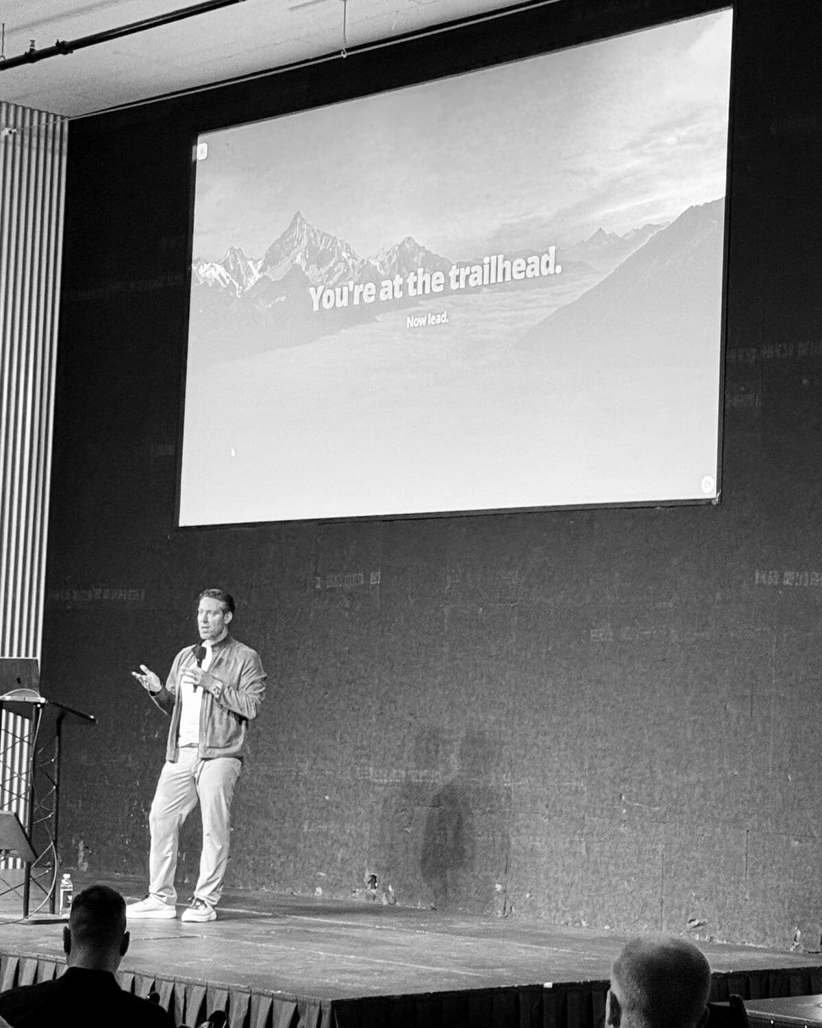 Colin Cox on stage beside a slide reading: You're at the trailhead. Now lead.